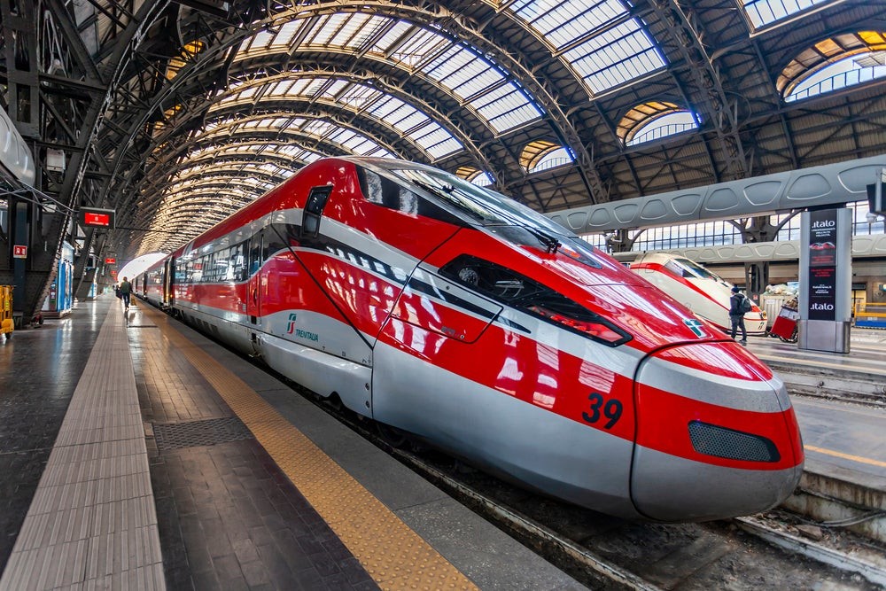 A Frecciarossa 1000 train speeds through the Italian countryside, showcasing its sleek design
