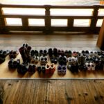 A view from above of dozens of pairs of shoes on a mat laid on a wooden floor, showcasing the importance of slip-on shoes in Japan