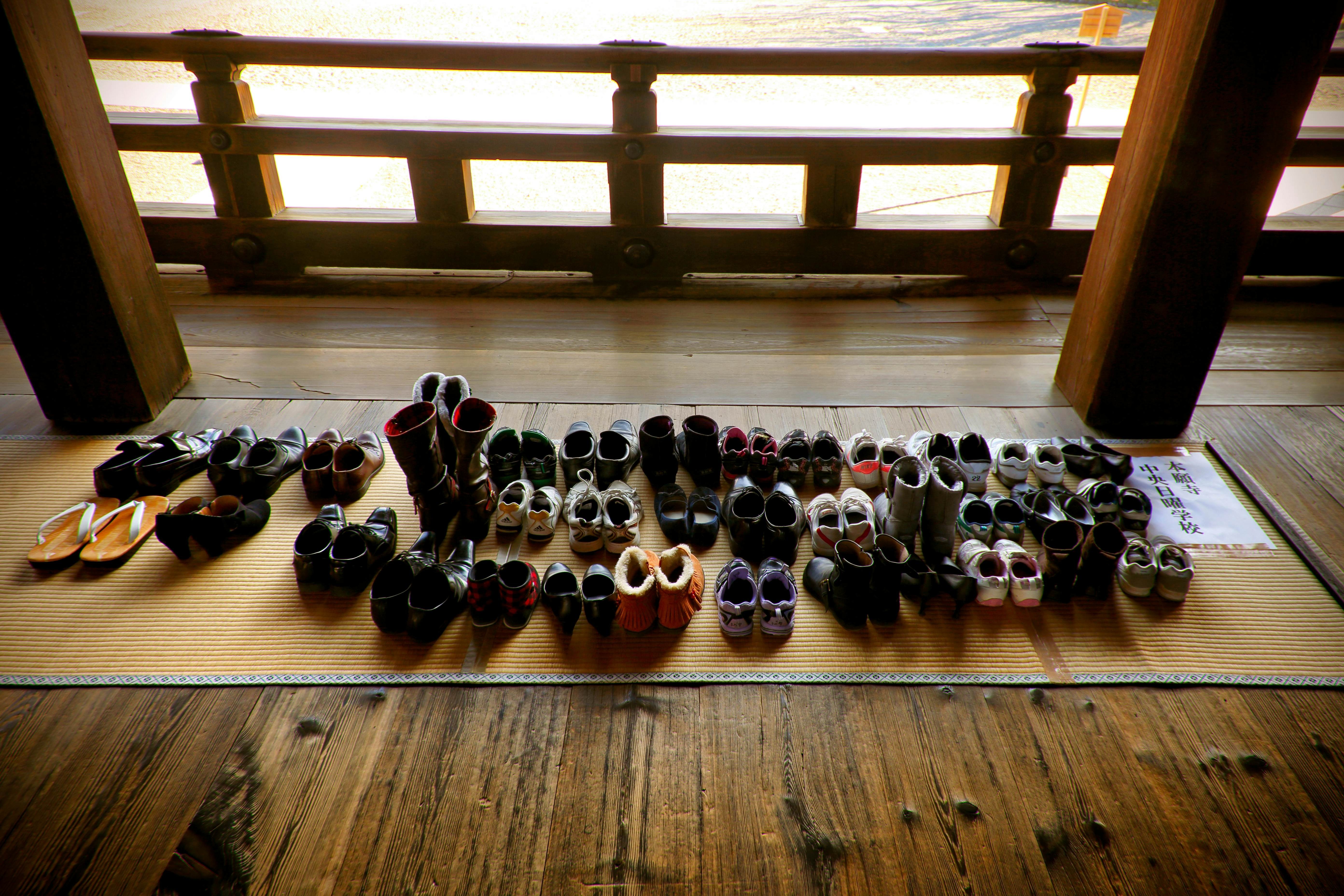 A view from above of dozens of pairs of shoes on a mat laid on a wooden floor, showcasing the importance of slip-on shoes in Japan