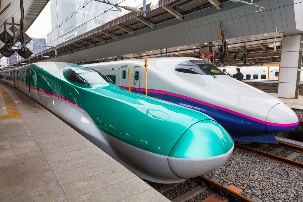 A Japanese Shinkansen bullet train elegantly speeds through the countryside, showcasing its iconic design