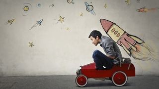 Person sitting in a toy car with space drawings, alt=Image of a child in a toy car, playfully imagining a drive to the moon amidst drawings of spaceships and planets.