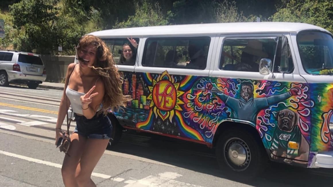 A traveler smiling in front of a classic hippie van in California