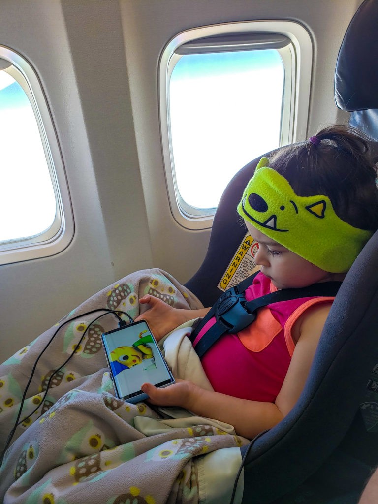 Toddler in car seat on airplane watching a phone