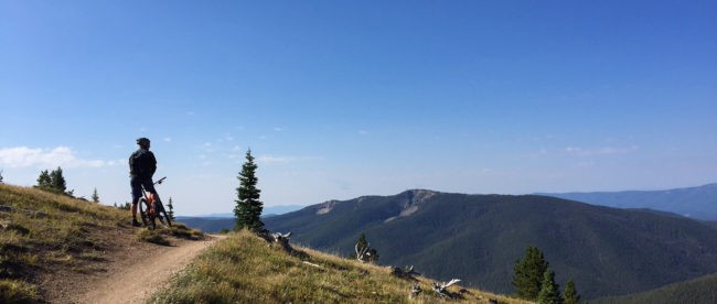 A motorcycle effortlessly conquers the summit, revealing a picturesque landscape of rolling hills and clear blue skies.
