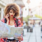 Woman traveler consults a map while standing on a city street.