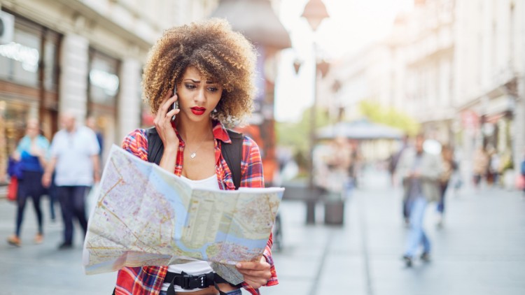 Woman traveler consults a map while standing on a city street.