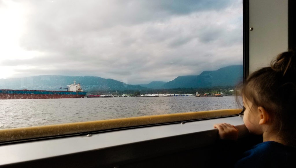 Toddler looking out of ferry at cargo boats in Vancouver Harbor