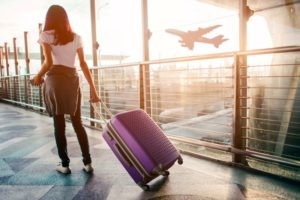 Woman walking through airport dragging suitcase, looking apprehensive, wondering if it's safe to travel after tooth extraction